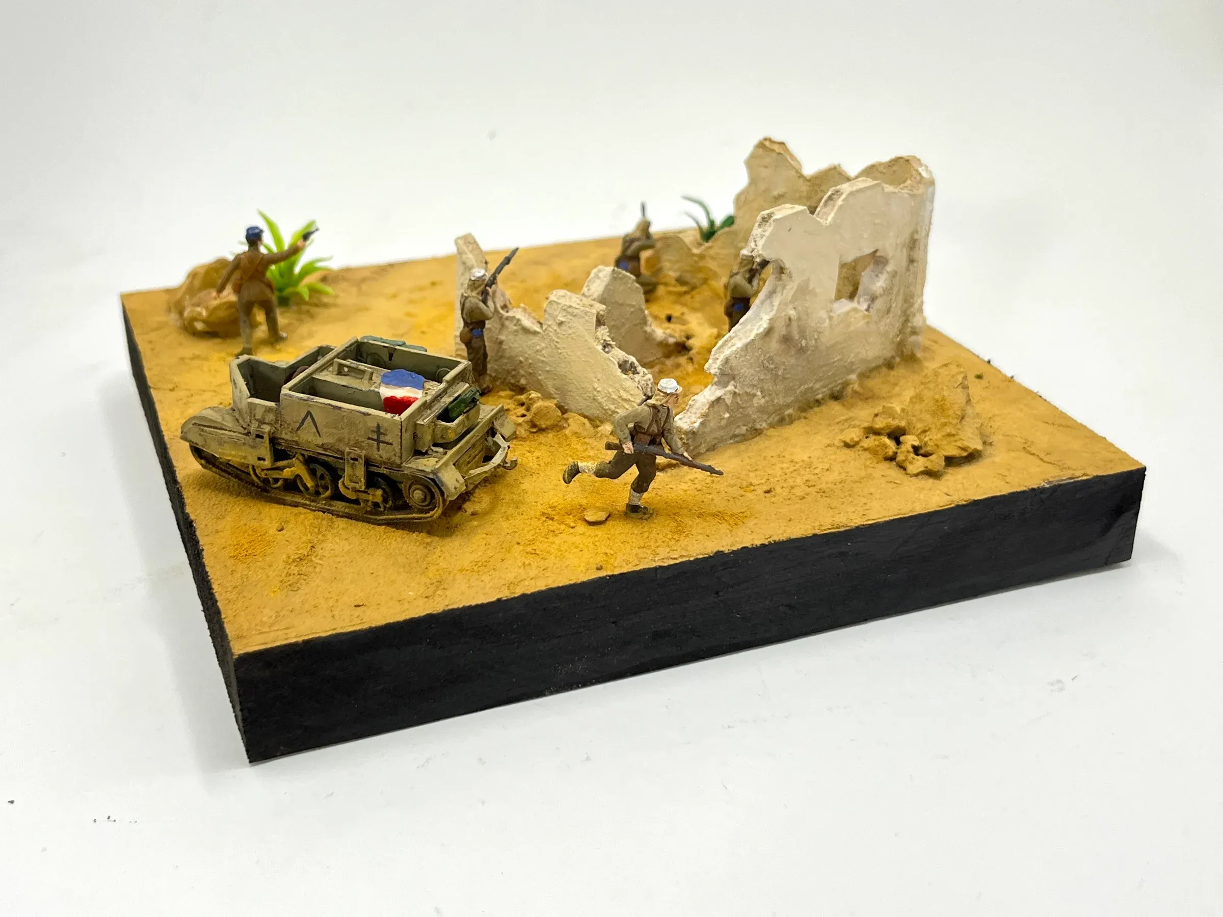 Diorama : un véhicule léger et des soldats au pied d’un mur en ruine, dans le sable