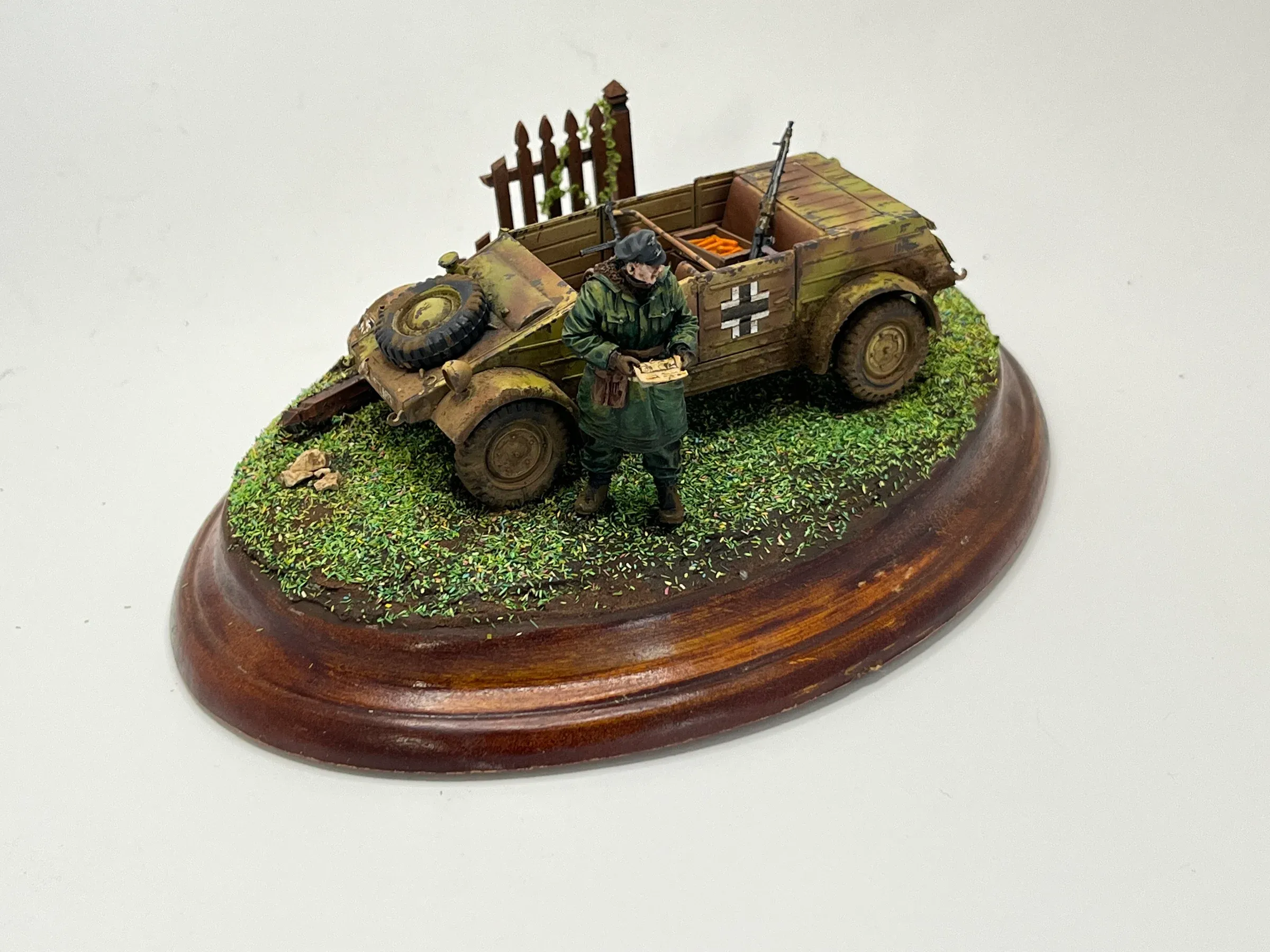 Diorama sur socle ovale en bois : un soldat allemand en manteau devant une voiture tout-terrain, près d’une barrière de bois