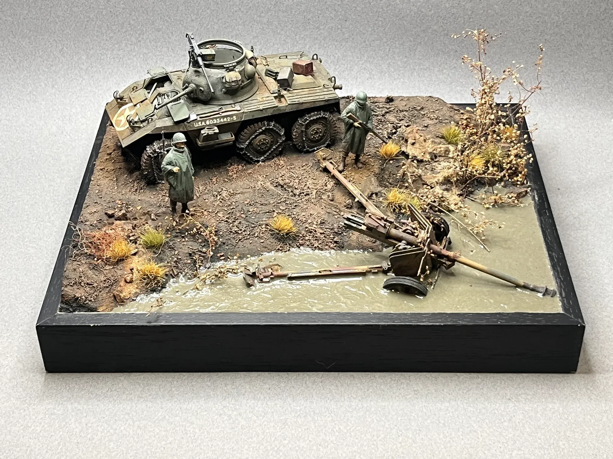 Diorama : une automitrailleuse américaine M8 et des soldats au bord d’une rivière, un canon abandonné dans l’herbe sèche