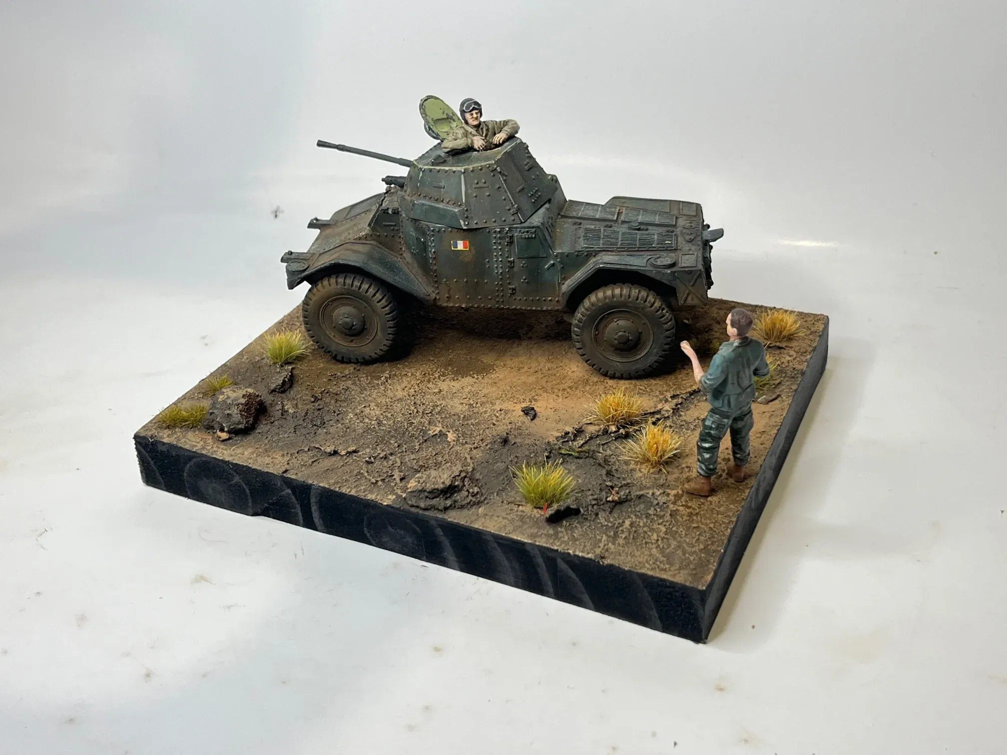 Diorama : une automitrailleuse et son équipage sur une piste caillouteuse, un soldat à pied fait signe au tireur