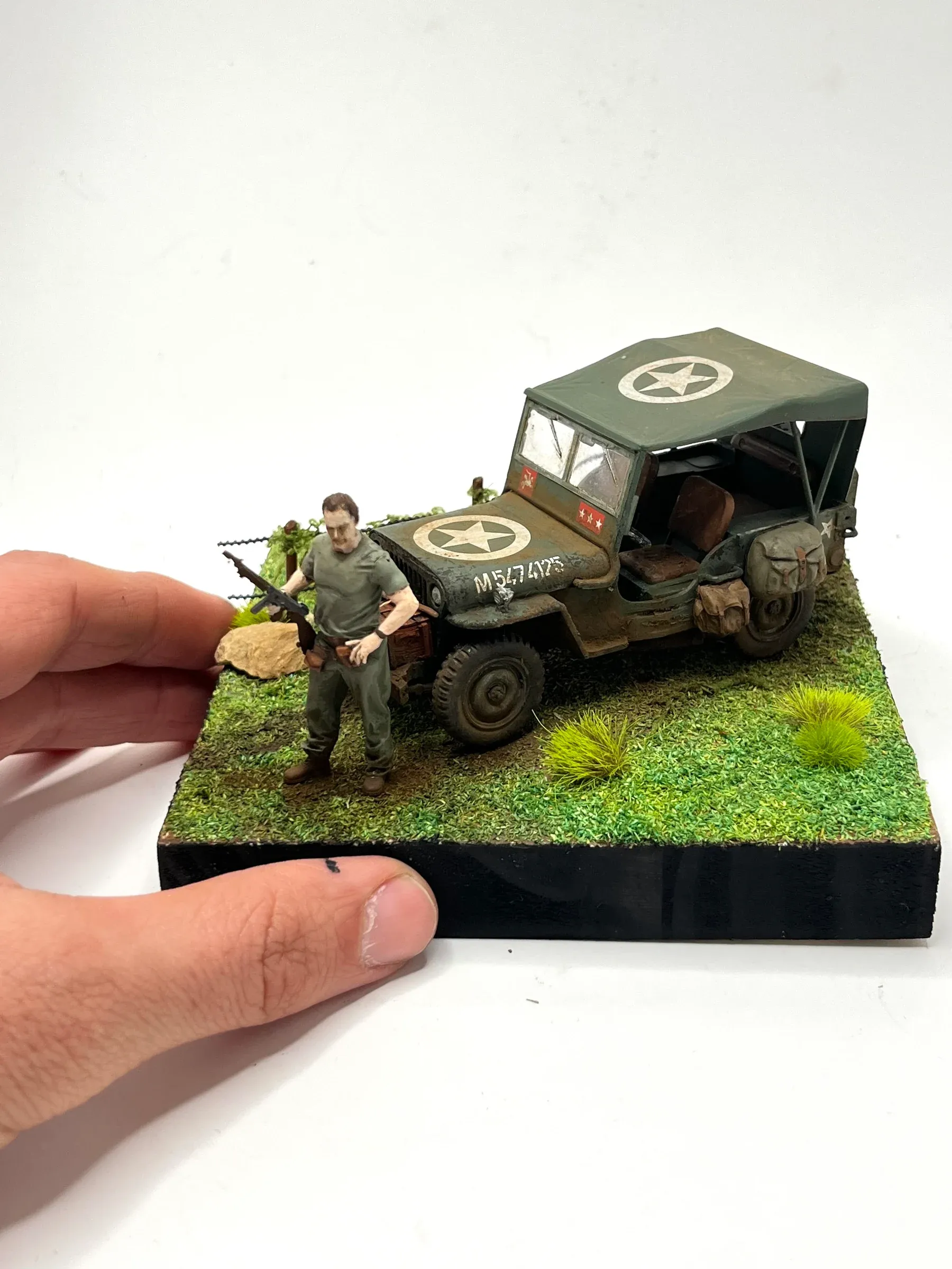 Petit diorama tenu en main : une jeep américaine bâchée et un soldat debout sur l’herbe