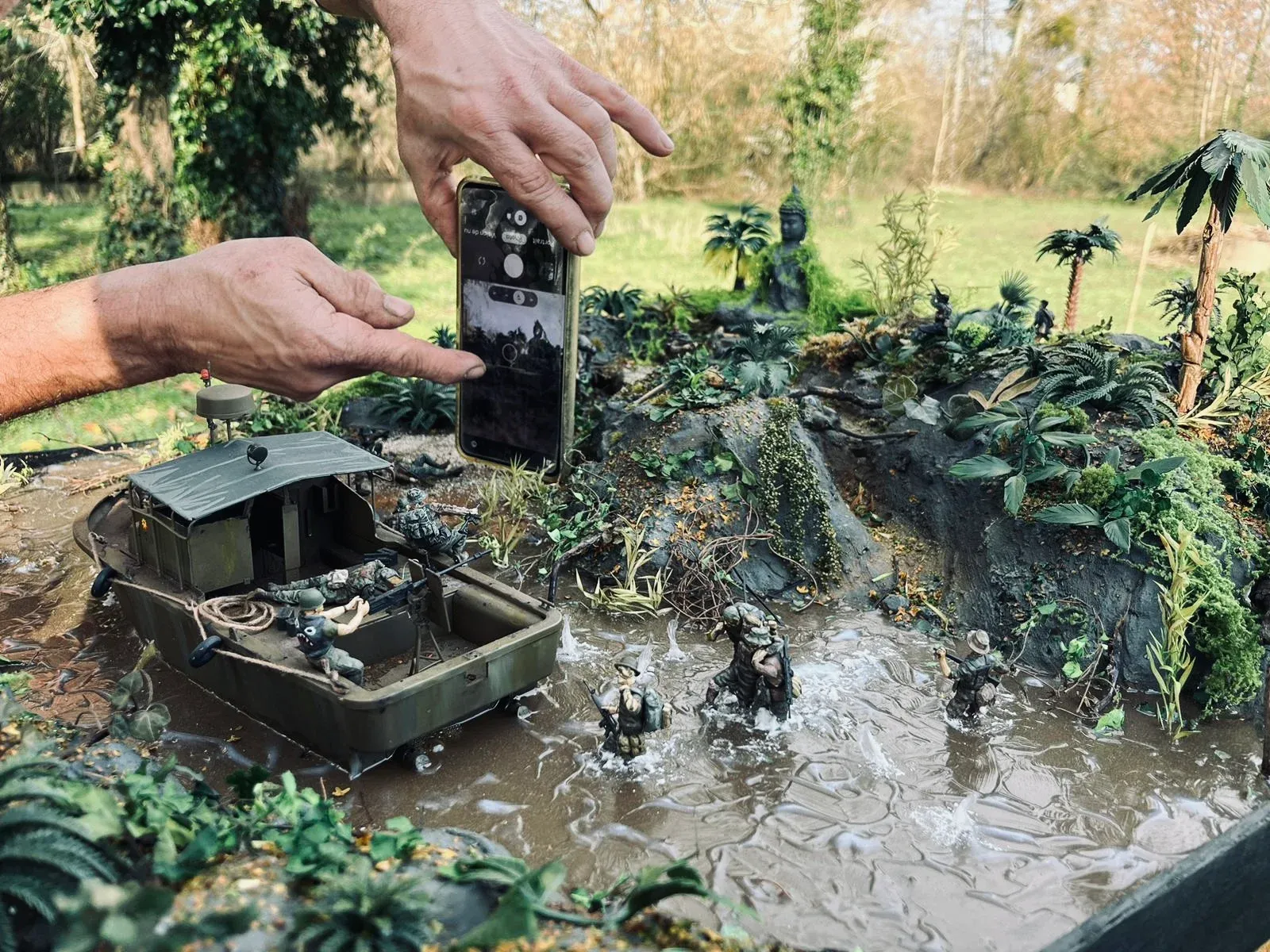 Prise de vue du diorama en extérieur, smartphone en main, au-dessus du patrouilleur fluvial et des fantassins dans l’eau boueuse