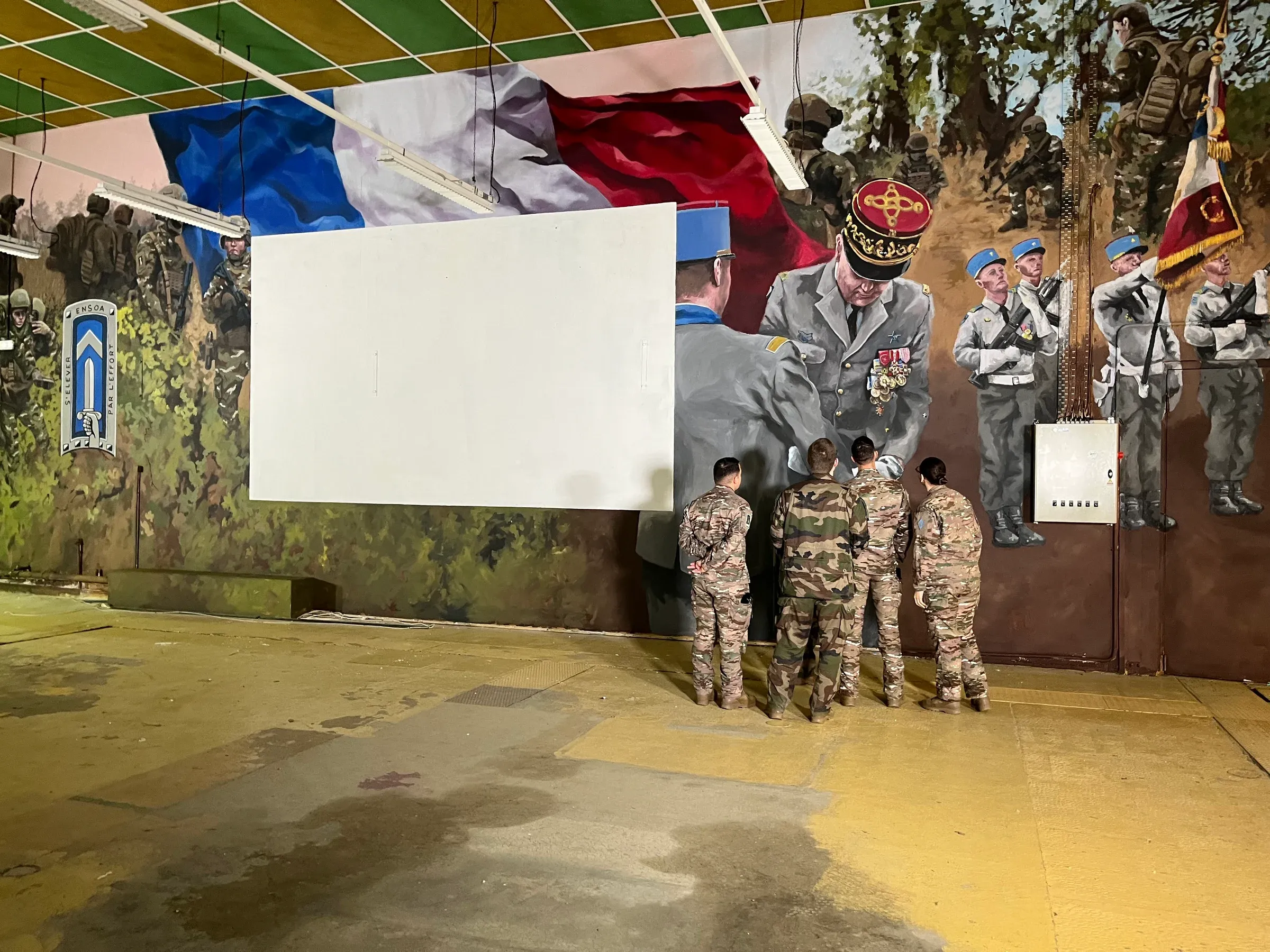 Élèves et cadres de l’ENSOA devant la fresque : drapeau tricolore, portraits d’officiers et soldats peints