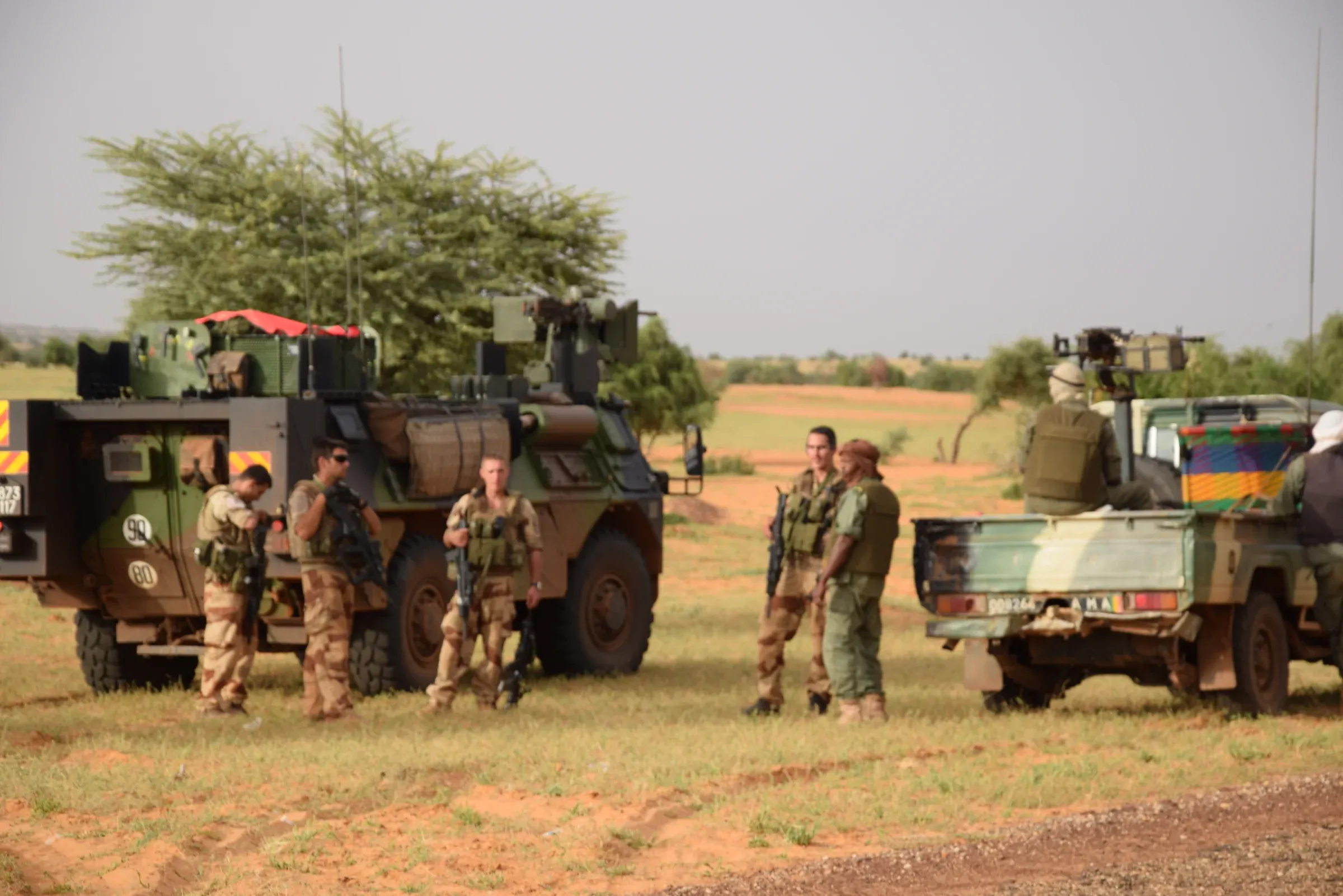 Photo de terrain : des soldats français près de véhicules blindés, sur une piste de terre rouge bordée d’arbres