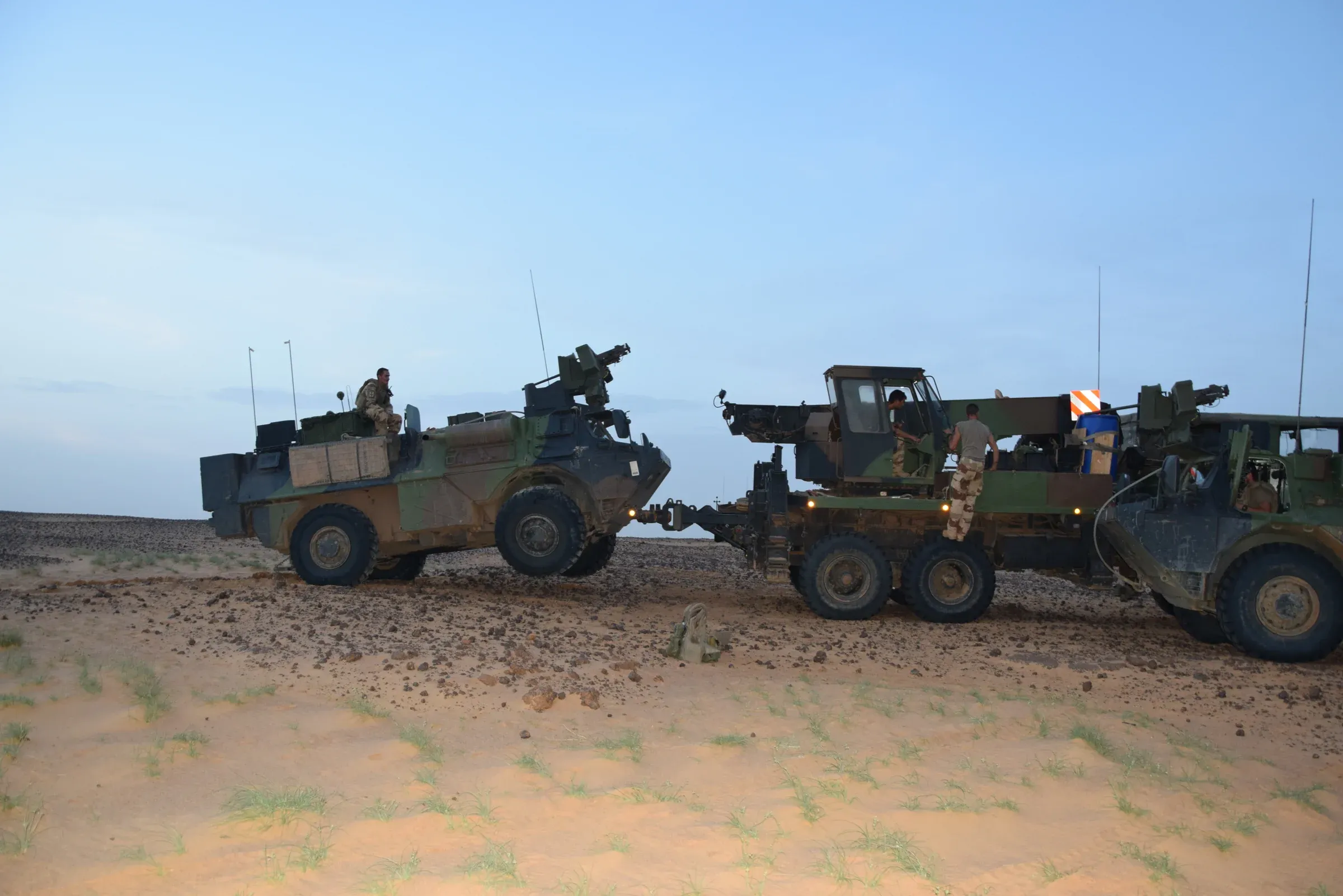 Photo de terrain : des véhicules militaires à l’arrêt dans le désert, sous un ciel bleu pâle