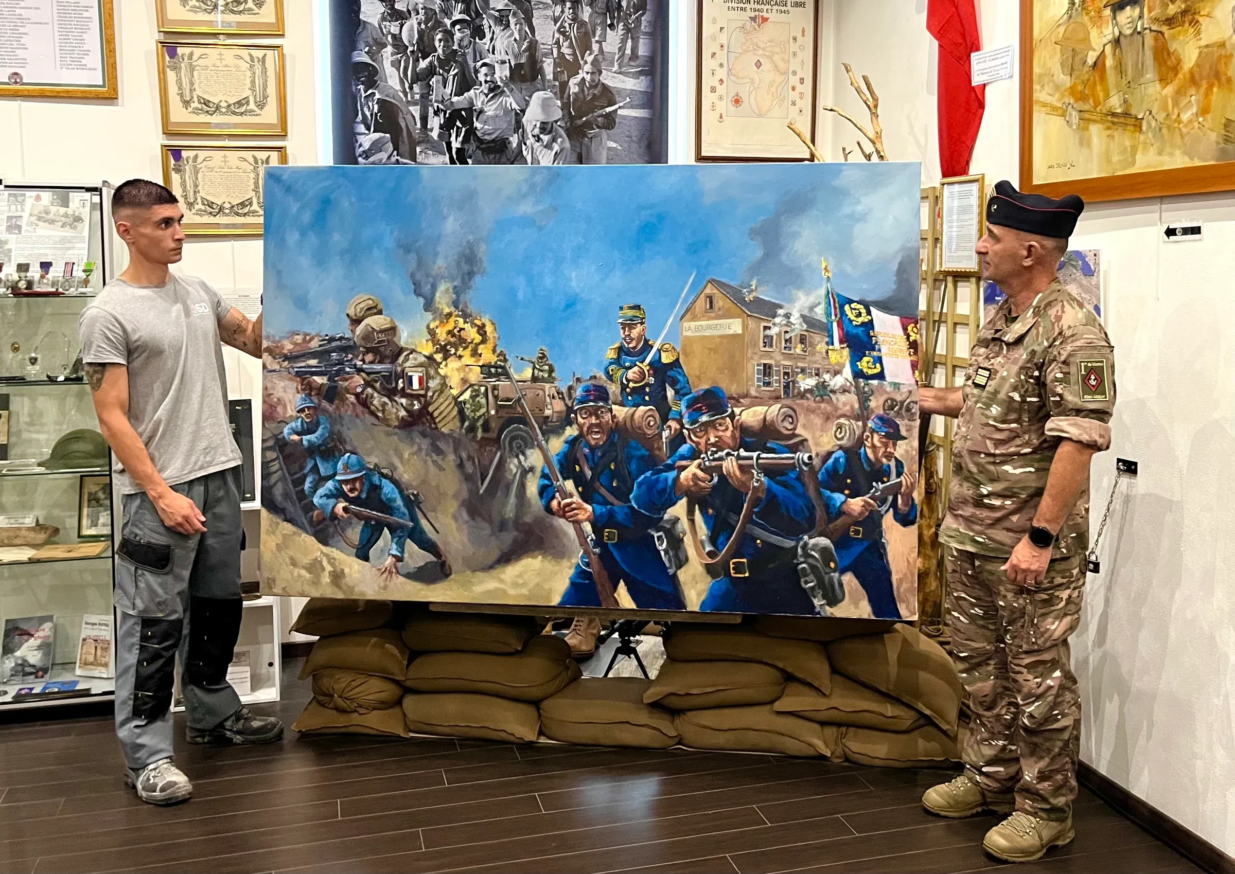 Le tableau présenté au 1er RIMa, posé sur des sacs de sable, entre deux hommes