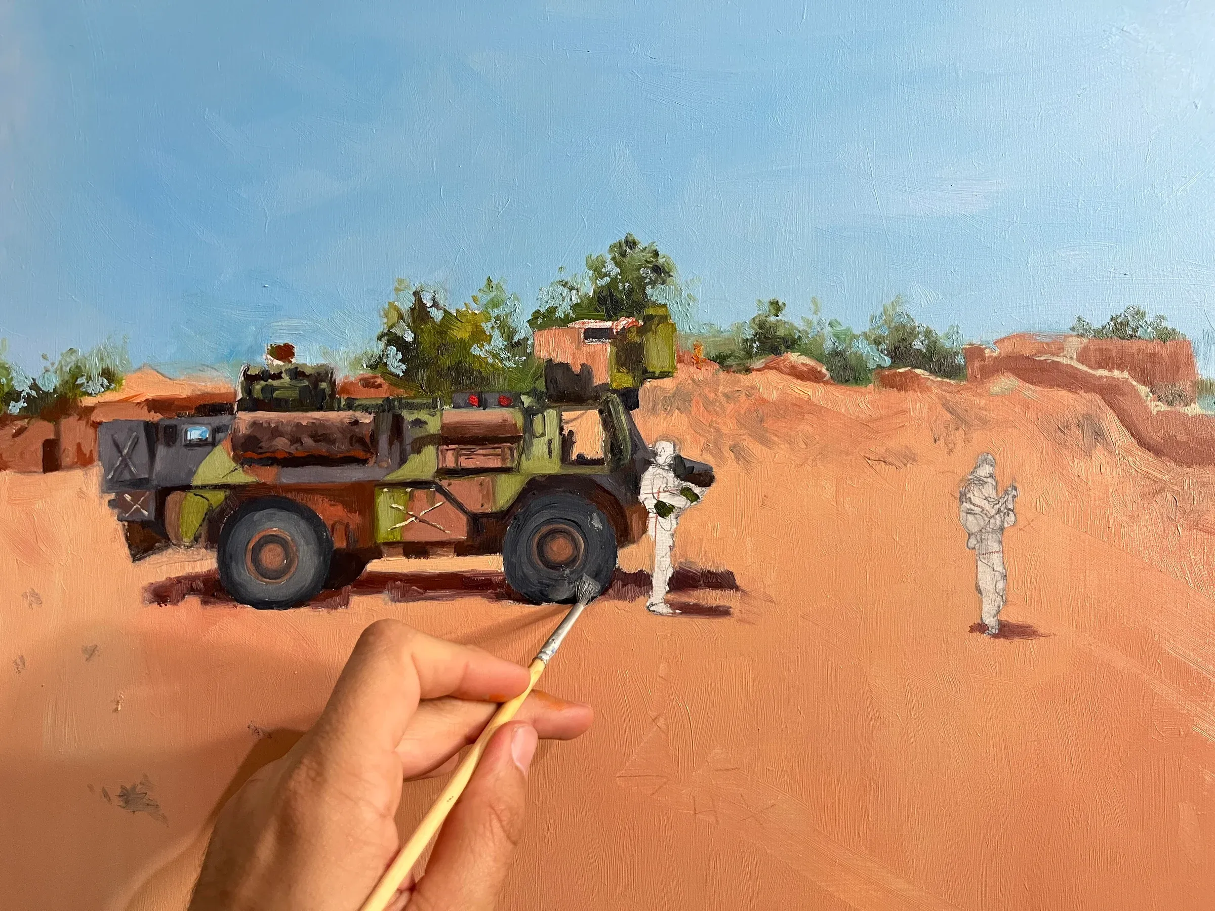 Le tableau en cours de réalisation : le pinceau pose les détails d’un véhicule blindé sur une piste de sable rouge