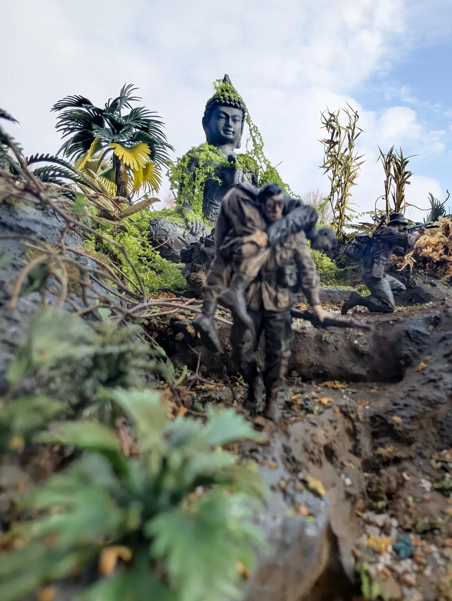 Détail : un fantassin dans la boue, devant une statue de Bouddha envahie par la végétation