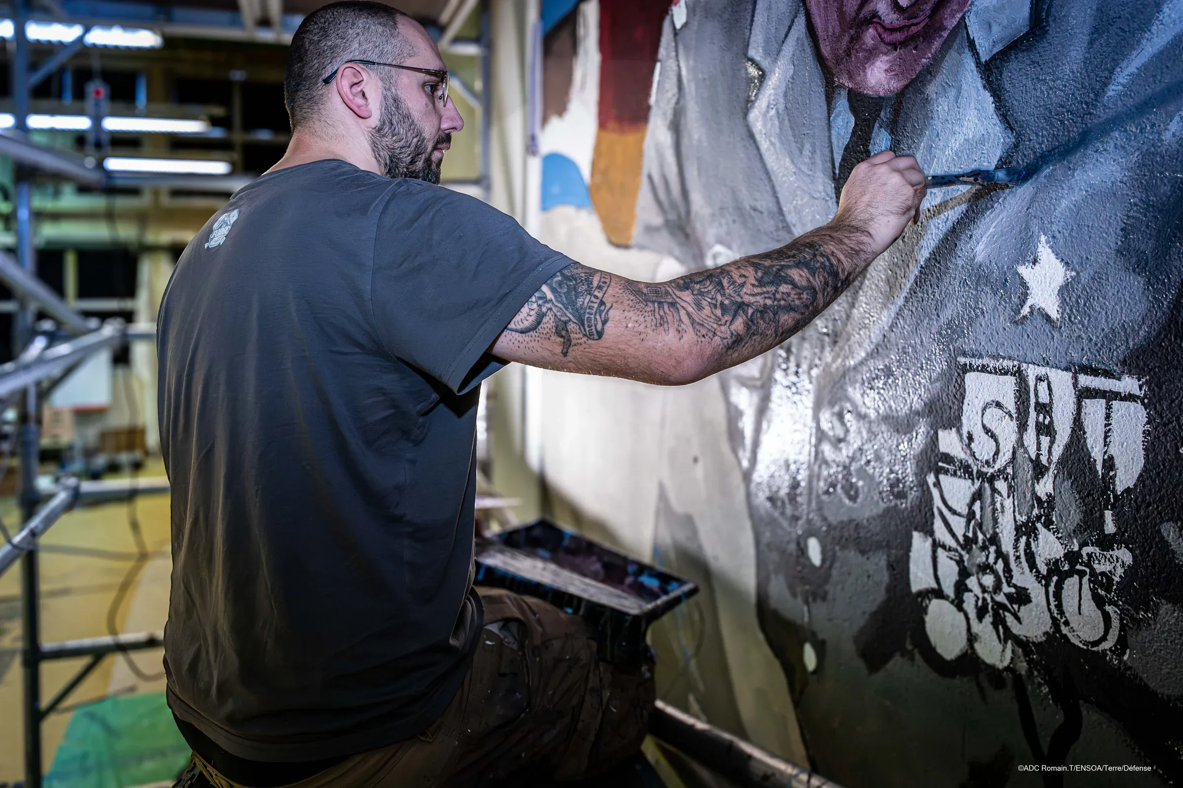 Au travail sur un mur de l’ENSOA, pinceau en main, devant le portrait d’un officier