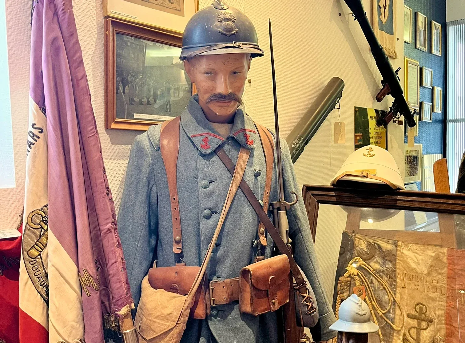 Un mannequin en uniforme bleu horizon de la Grande Guerre, entouré de drapeaux, d’armes et de souvenirs