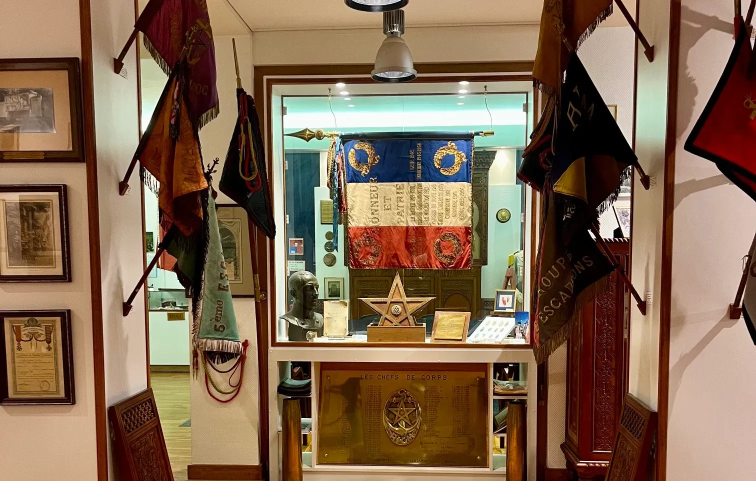 Une salle d’honneur : un drapeau sous vitrine, entouré de fanions et de souvenirs encadrés